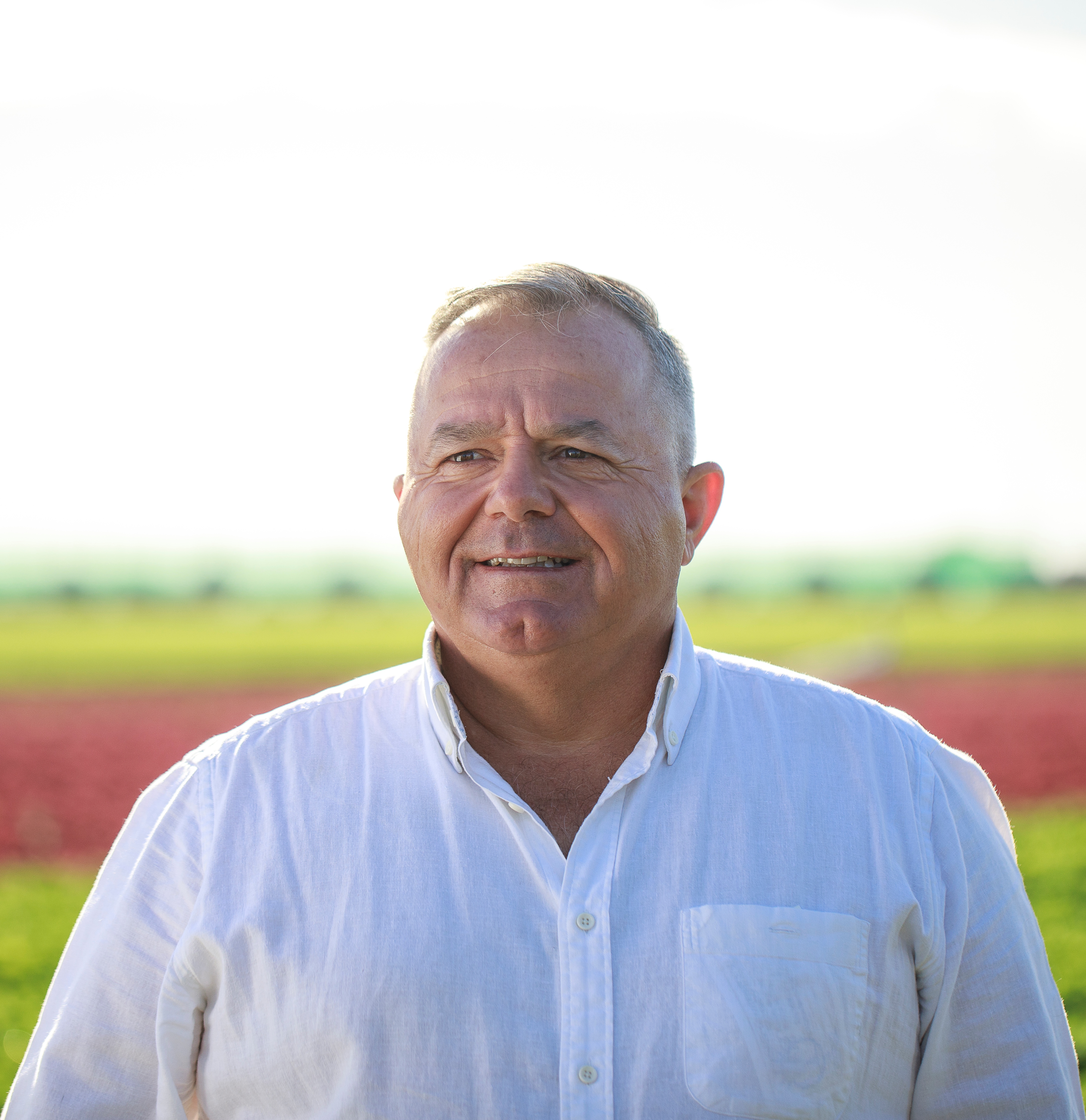 headshot of man in white shirt with blurred farmland background